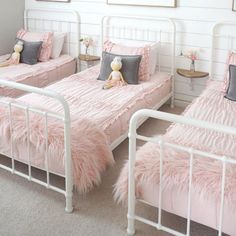 three beds with pink bedding and pillows in a white walled room, one has a teddy bear on it