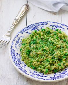 a white and blue plate topped with green food next to a fork, knife and napkin