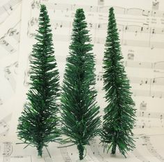 three small green christmas trees sitting on top of sheet music paper with musical notes in the background