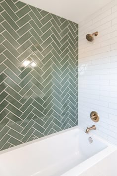 a white bath tub sitting next to a green tiled bathroom wall with gold faucet