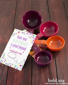 colorful measuring cups and spoons on a wooden table with a happy birthday card next to them