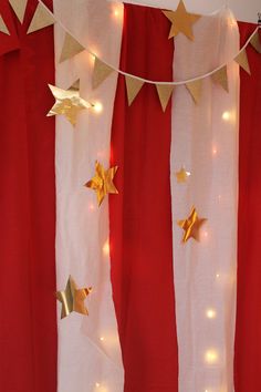 red and white curtains with gold stars hanging from the top, along with string lights