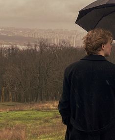 a woman standing in the rain with an umbrella over her head, looking out at a city