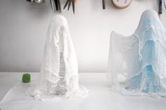 two sculptures made out of cloths on top of a white table next to clocks