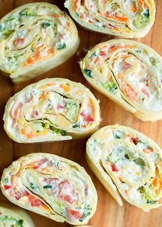 several rolls filled with vegetables and cheese on top of a wooden table next to a fork