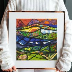 a person holding up a painting with mountains in the background