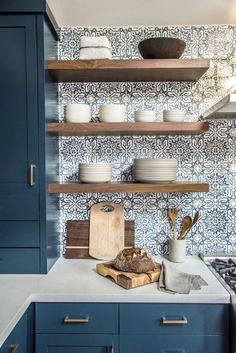 a kitchen with blue cabinets and open shelving above the stove top is filled with dishes