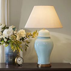 a blue vase with white flowers and a clock on a table next to a lamp