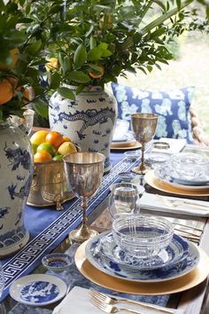 an outdoor table set with blue and white china, oranges and lemons in vases