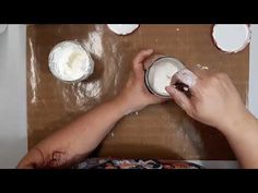 a person is spreading white icing on some cake batter in a bowl and another hand is holding a spoon