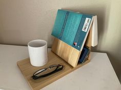 a wooden desk with a cup, glasses and book on it next to a pair of reading glasses