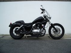 a black motorcycle parked on the side of a road next to a white wall and building