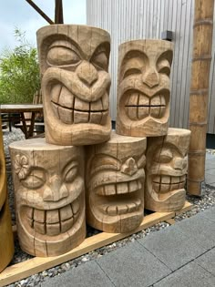 four carved wooden tiki heads on display in front of a building with gravel and rocks