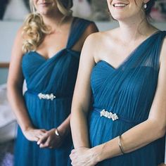 two women in blue dresses standing next to each other and smiling at the same time