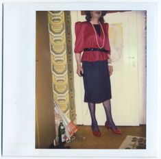 an old photo of a woman standing in front of a door wearing a red blouse and black skirt