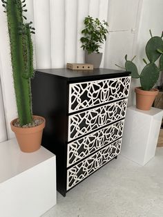 a black and white dresser next to a cactus in a potted houseplant