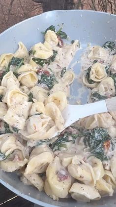 a pan filled with pasta and spinach on top of an oven burner,