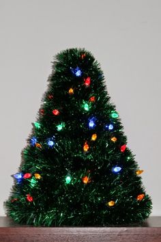 a small christmas tree with multicolored lights in a wooden box on a table