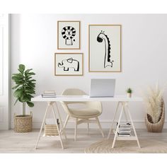 a white desk with a laptop on it in front of three framed pictures and a potted plant