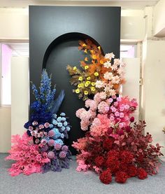 there are many different colored flowers on the floor in front of a large black wall