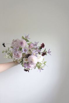 a woman holding a bouquet of flowers in her hand on a white wall with sunlight coming through the window