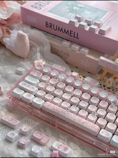 a pink and white keyboard sitting on top of a table next to a book with the word brummel written on it