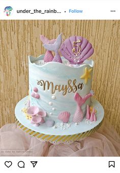 a blue and pink cake with mermaid decorations on it's top, sitting on a table