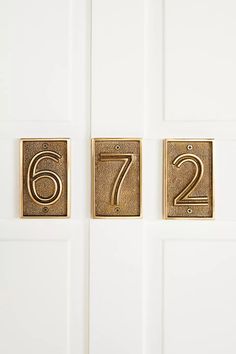 two brass numbers on the front door of a house with white walls and doors in the background