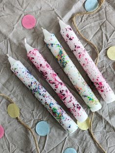 three white candles with sprinkles and confetti on the table next to them