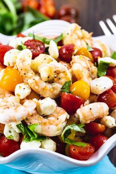 a white bowl filled with shrimp, tomatoes and feta cheese salad on top of a blue napkin