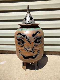 a large metal pot with a face painted on it's side sitting in front of a garage door