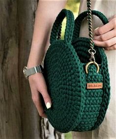 a woman holding a green crocheted purse with a chain around the strap and clasp