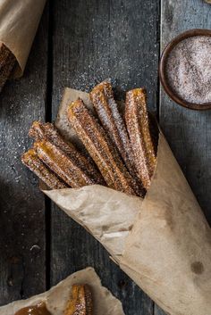 some churros are sitting on top of brown paper and next to cinnamon sugar