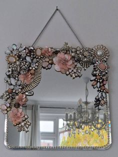 a mirror hanging on the wall with flowers and pearls around it's edges in front of a chandelier