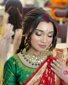 a woman wearing a green and red sari with gold jewelry on her neck, holding a