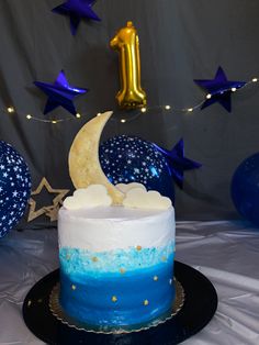 a blue and white cake sitting on top of a black plate next to balloons in the shape of stars