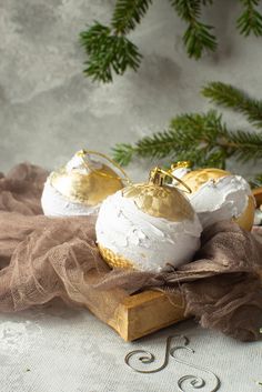 two white and gold ornaments sitting on top of a piece of cloth next to evergreen branches