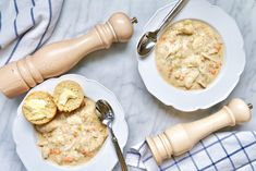 two white plates filled with food next to a wooden spoon and fork on top of a table