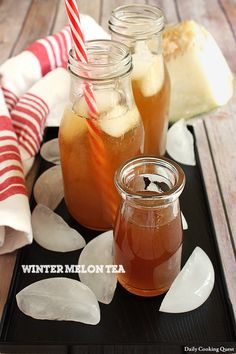 three mason jars filled with iced tea sit on a black tray next to ice and candy canes