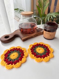 two crocheted coasters sitting on top of a table next to a jar of tea