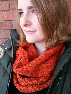 a woman wearing an orange knitted scarf in front of a brick wall with her head tilted to the side