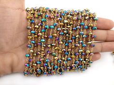 a hand is holding a gold chain bracelet with multicolored beads and chains on it