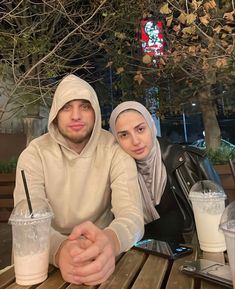 two people sitting at a table with drinks in front of them and one person wearing a headscarf