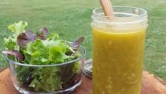 a glass jar filled with green liquid sitting next to a salad on a wooden table