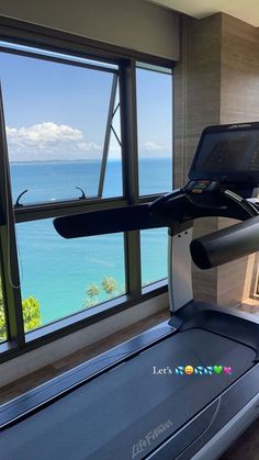 there is a treadmill in front of a window overlooking the ocean and water with an open laptop on it