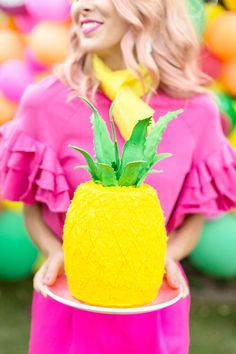 a woman in a pink dress holding a yellow pineapple