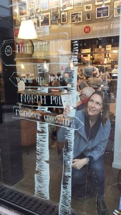 a woman sitting in front of a store window holding up a sign that says north pole