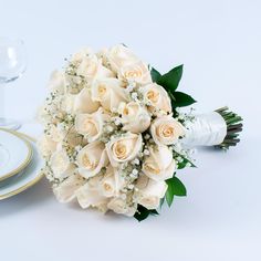 a bouquet of white roses sitting on top of a table next to a wine glass