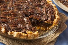 a pecan pie on a plate with a slice taken out of it and sitting on a burlap cloth