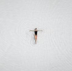 a woman in a black swimsuit floating on top of the water with her arms spread out